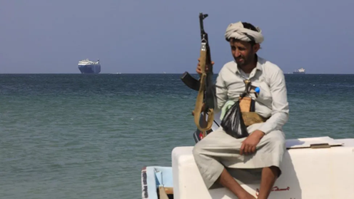 An armed Yemeni sits on a boat in front of the Galaxy Leader cargo ship last month